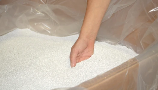 Hand reaching into a box of white elastomers and plastomers